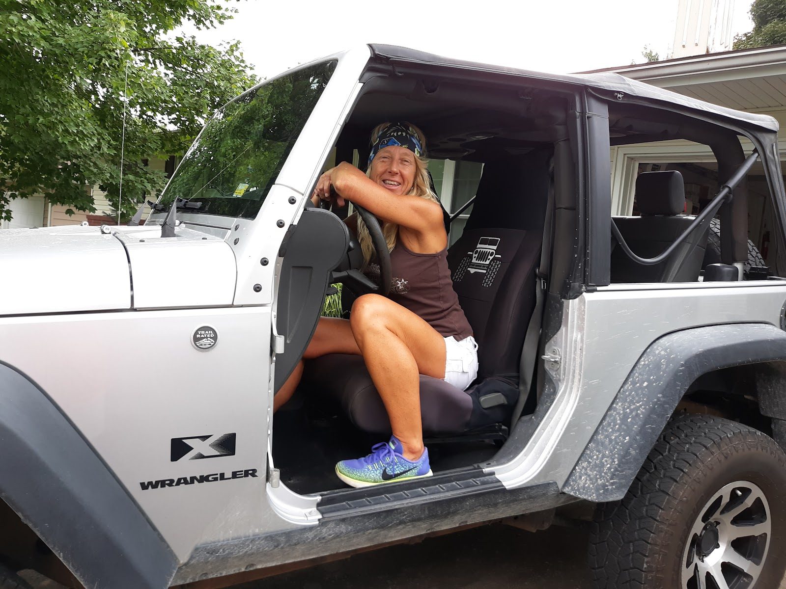A smiling driver in a silver Jeep Wrangler with the door open