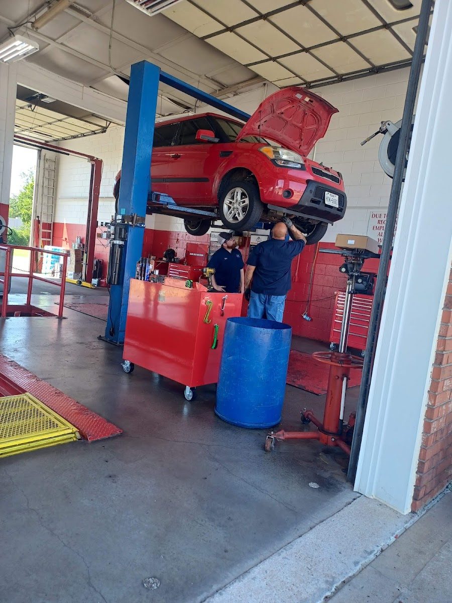 Two mechanics working under a red car up on the lift